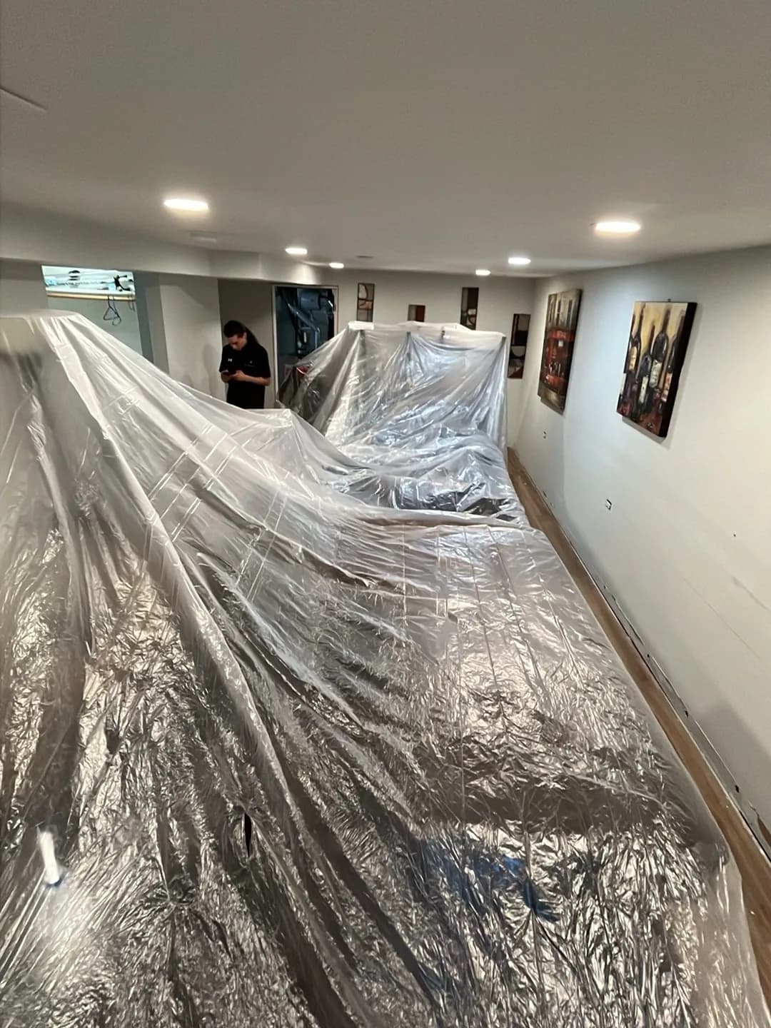 Finished basement wrapped in protective sheeting, with a technician working inside.